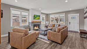 A spacious living room with a stone fireplace, leather sofas, and large windows. - Tucked Away Paradise (Coeur d'Alene)