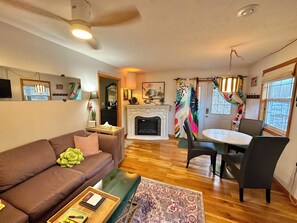 A cozy living room with a fireplace, a dining area with a table and chairs, and a large window.