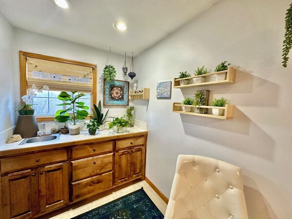 A bathroom with wooden cabinets, a sink, and a mirror. There are potted plants on the counter and shelves on the wall.