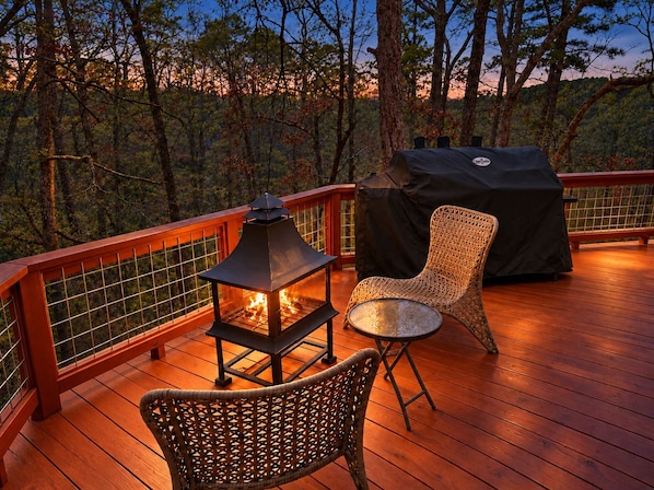 A deck with a fire pit, outdoor furniture, and a grill, surrounded by trees.