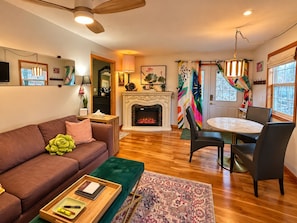 A living room with a fireplace, a sofa, a dining table with chairs, and a ceiling fan.
