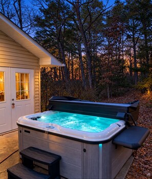 A hot tub with a bench, located outside a house with a door and windows.