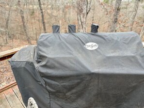 A Char-Griller grill with a protective cover, set against a backdrop of trees.