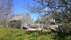 A rustic wooden building with a stone staircase leading to a dock over a body of water, surrounded by lush greenery and a clear blue sky.