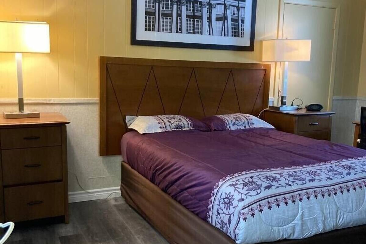 A bedroom with a wooden bed, two bedside tables, a nightstand, a framed picture on the wall, and a door.