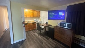 A compact kitchen with wooden cabinets, a stove, a microwave, and a television displaying a welcome message. - Pine Ridge Motel (Timmins)