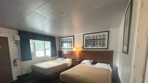 A hotel room with two single beds, a window with curtains, a wall-mounted lamp, and framed pictures. - Pine Ridge Motel (Timmins)
