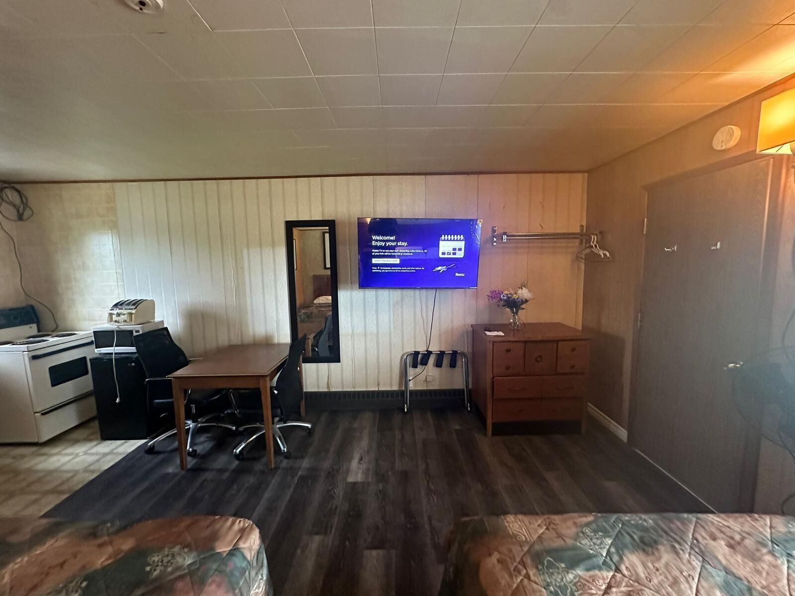 Camera d'albergo con angolo cottura, scrivania, sedia, specchio, televisore, cassettiera e un letto.