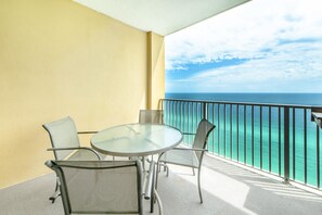En balkon med et glasbord og stole, med udsigt over et turkis hav.