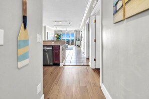 A hallway with wooden flooring, a kitchen area with a counter and cabinets, and a view to a balcony.