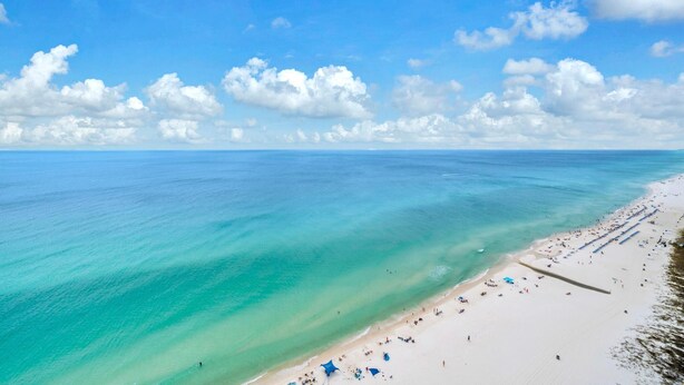 A beach with clear turquoise water, a sandy shore, and a few umbrellas. - Tropic Winds 2308 (Panama City Beach)