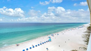 A beach with a row of blue umbrellas, a sandy shore, and the ocean. - Tropic Winds 1104 (Panama City Beach)