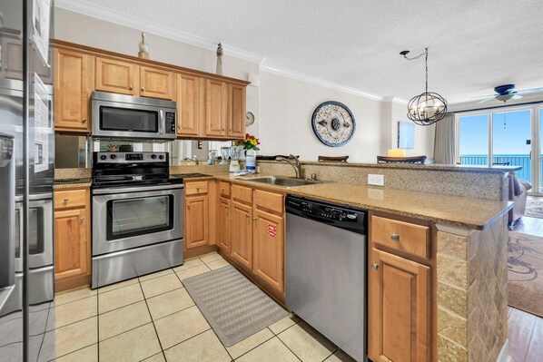 A kitchen with stainless steel appliances, wooden cabinets, a granite countertop, and a view of the balcony. - Tropic Winds 1104 (Panama City Beach)