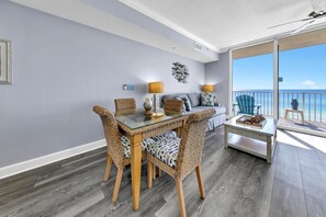 A modern living room with a glass dining table, wicker chairs, a sofa, and a balcony with a view of the ocean. - Tidewater 314 NEW (Panama City Beach)