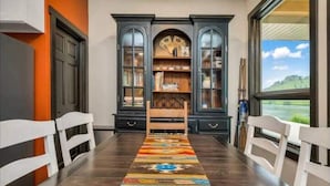 Un comedor con una mesa larga, sillas, un tapete estampado y una estantería con puertas de vidrio.