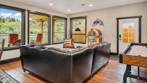 Un salón amplio con un sofá modular grande, una mesa de billar y amplias ventanas con vistas al exterior.