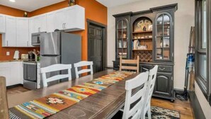 Una cocina con armarios blancos, un refrigerador y una mesa de comedor con sillas.