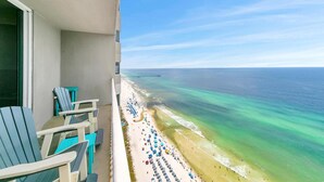A balcony with blue chairs and a view of a beach with a pier.