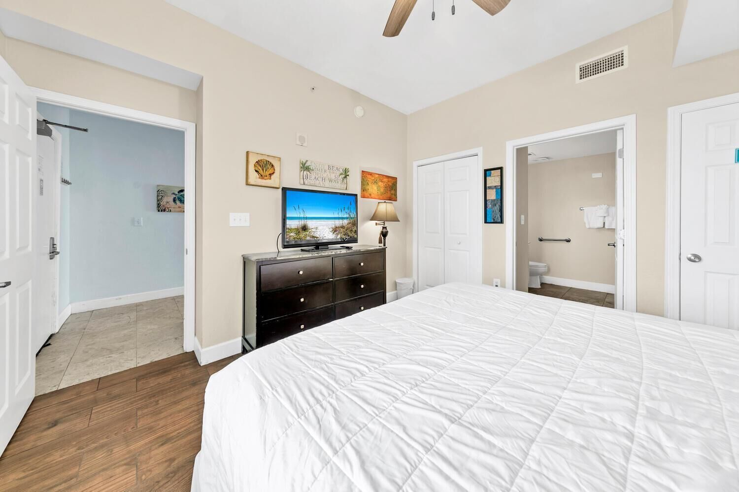 A bedroom with a large bed, a dresser, a television, and artwork on the wall.