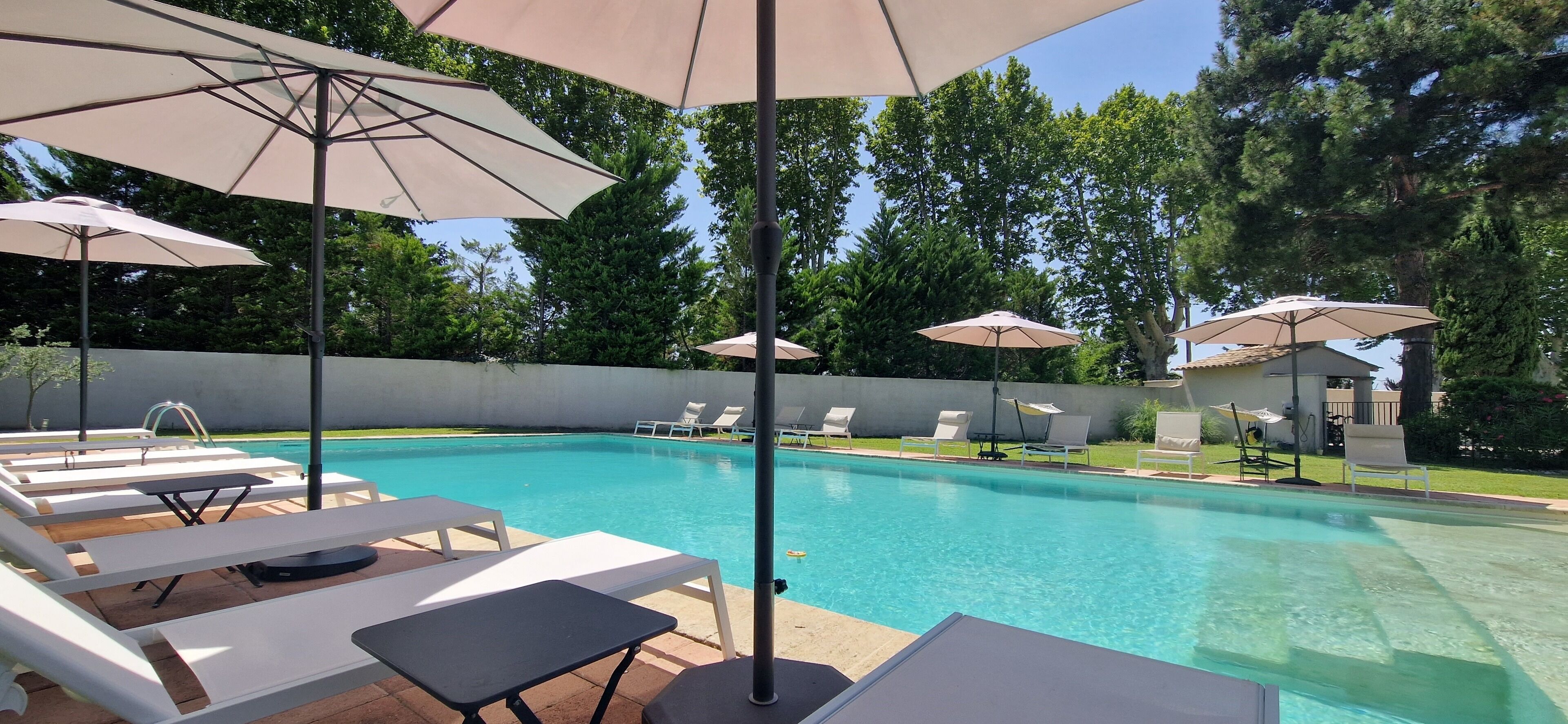 A swimming pool with lounge chairs and umbrellas, surrounded by a concrete wall and trees.