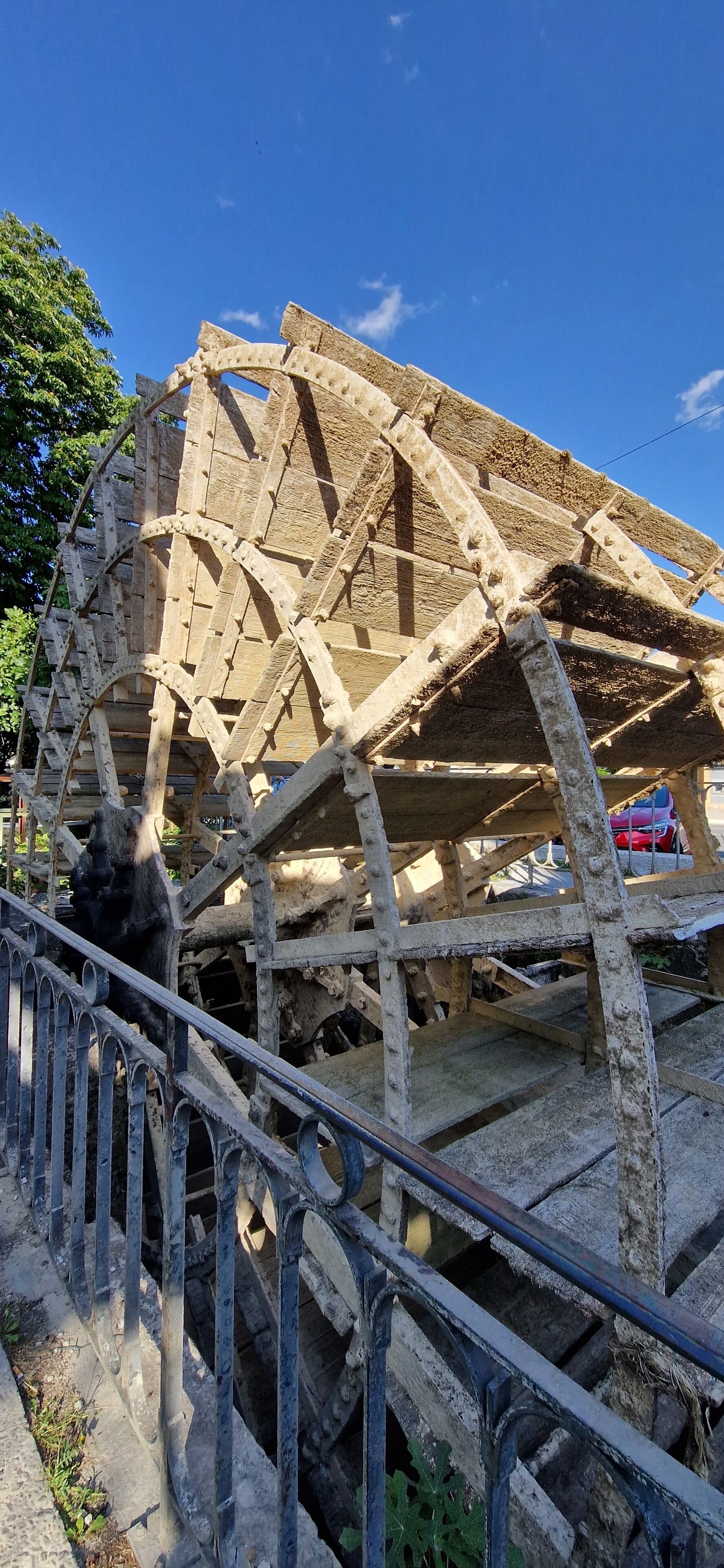 A large, historic water wheel structure with metal railings in the foreground.