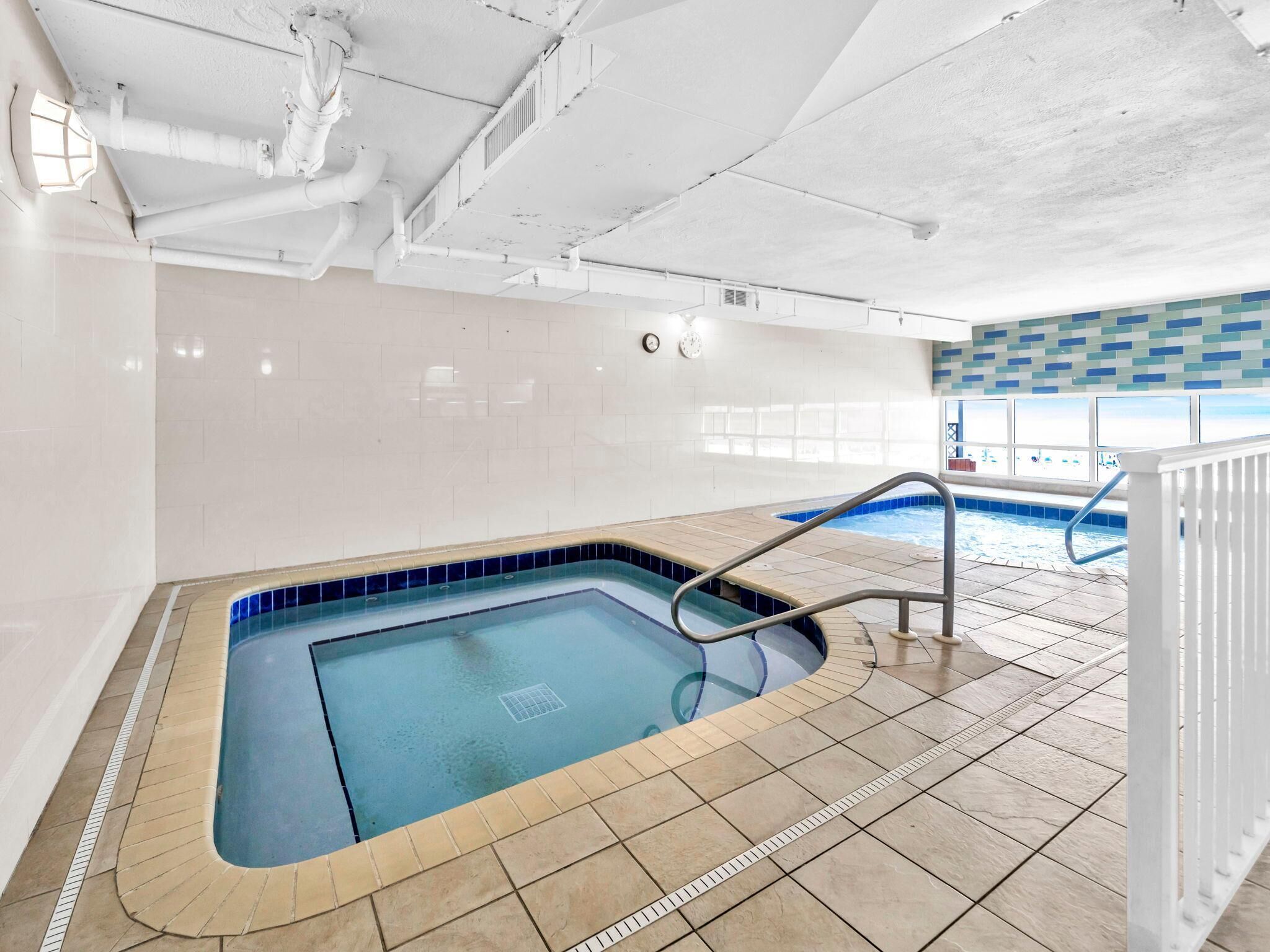 Una piscina interior con agua cristalina, suelo de baldosas y techo blanco con tuberías visibles.