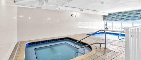 Una piscina interior con agua cristalina, suelo de baldosas y techo blanco con tuberías visibles.