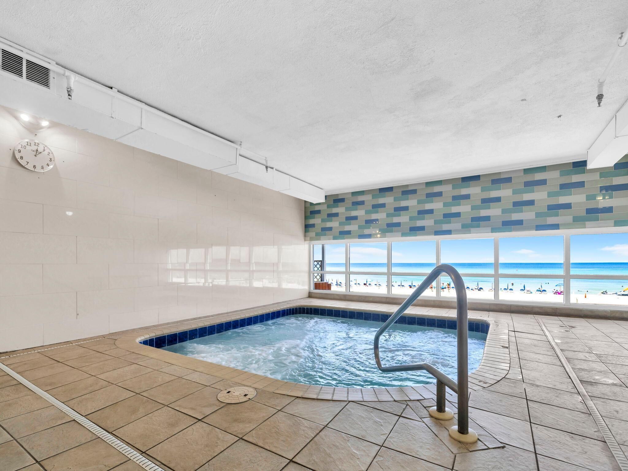 Una piscina interna con vista sulla spiaggia, pareti piastrellate e una sveglia appesa al muro.