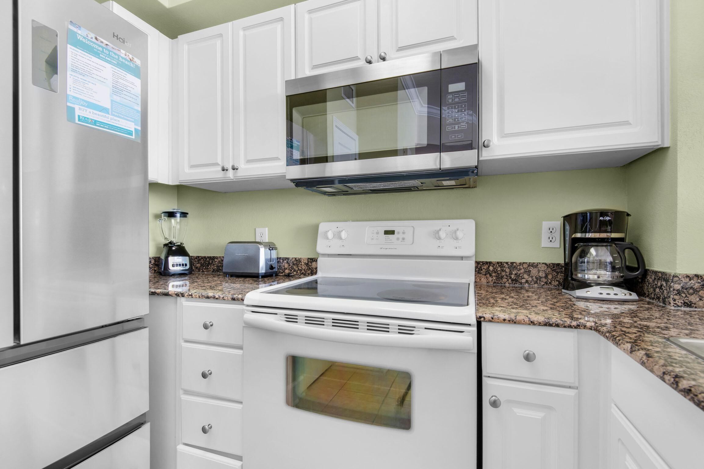 Una cocina con gabinetes blancos, un refrigerador de acero inoxidable, un microondas, una estufa y una cafetera.