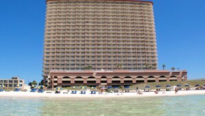 Un gran hotel con varios balcones, una zona de playa con sombrillas y agua azul cristalina.