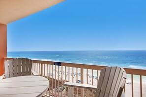 A balcony with a table and chairs, overlooking a beach with umbrellas and the ocean. - Sunrise Beach 910 (Panama City Beach)