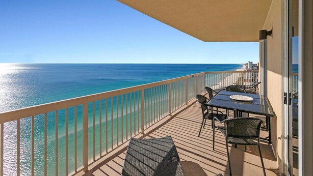 A balcony with a view of the ocean, a table with chairs, and a glass door. - Sunrise Beach 2411 (Panama City Beach)