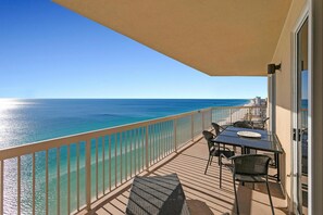 A balcony with a view of the ocean, a table with chairs, and a glass door. - Sunrise Beach 2411 (Panama City Beach)