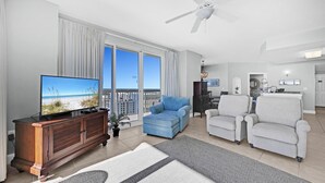 A modern living room with a television, blue and grey sofas, a wooden cabinet, and a large window with a view of the city. - Sunrise Beach 2411 (Panama City Beach)