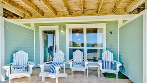 Eine überdachte Veranda mit vier Adirondack-Stühlen, jeder mit einem Kissen, und einem kleinen Tisch.