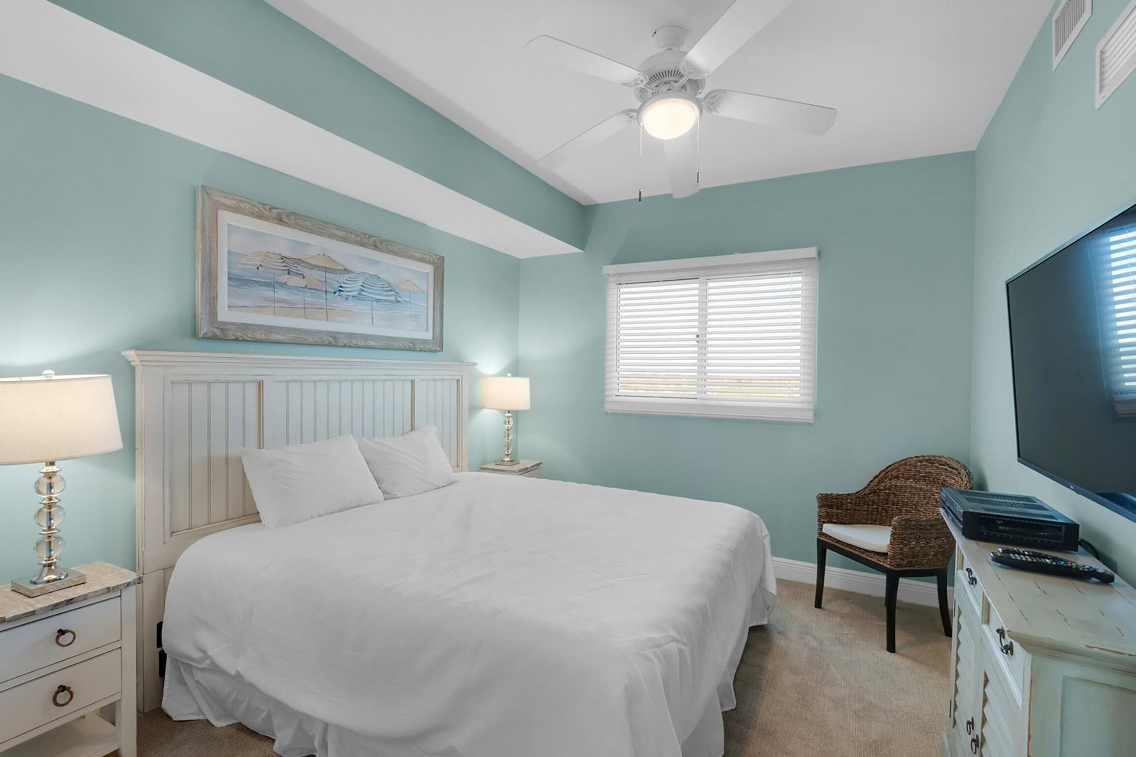 A bedroom with a bed, a ceiling fan, a television, and a window with blinds.