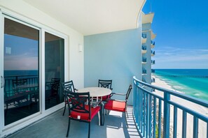 Un balcon avec une table et des chaises, donnant sur une plage et une jetée.