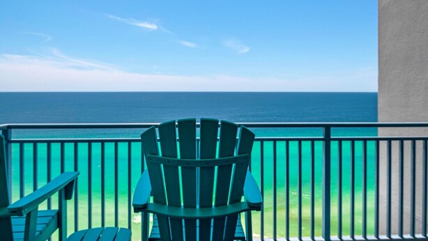 Een balkon met een groene Adirondack-stoel en een kleine tafel, met uitzicht op een heldere blauwe oceaan.