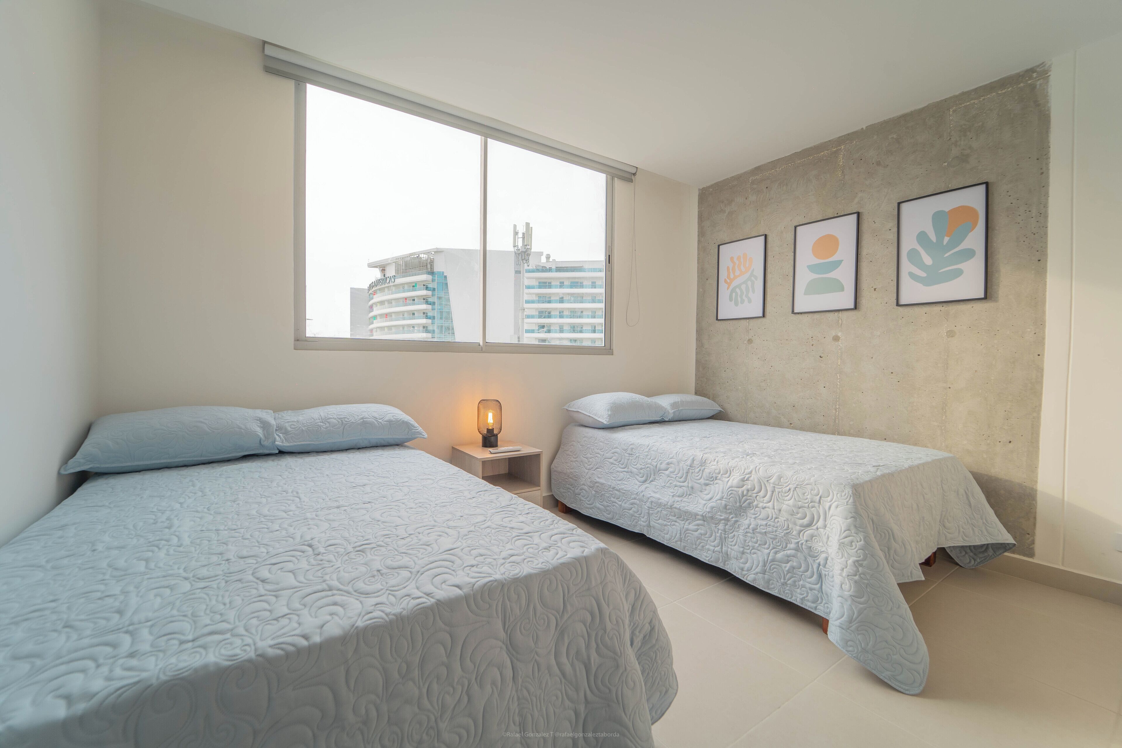 Un dormitorio con dos camas, una ventana y una mesita de noche con lámpara.