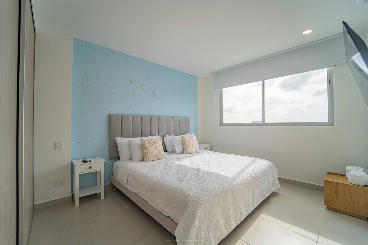 Une chambre moderne avec un grand lit, une table de chevet, une petite table en bois et une fenêtre donnant sur un beau paysage.