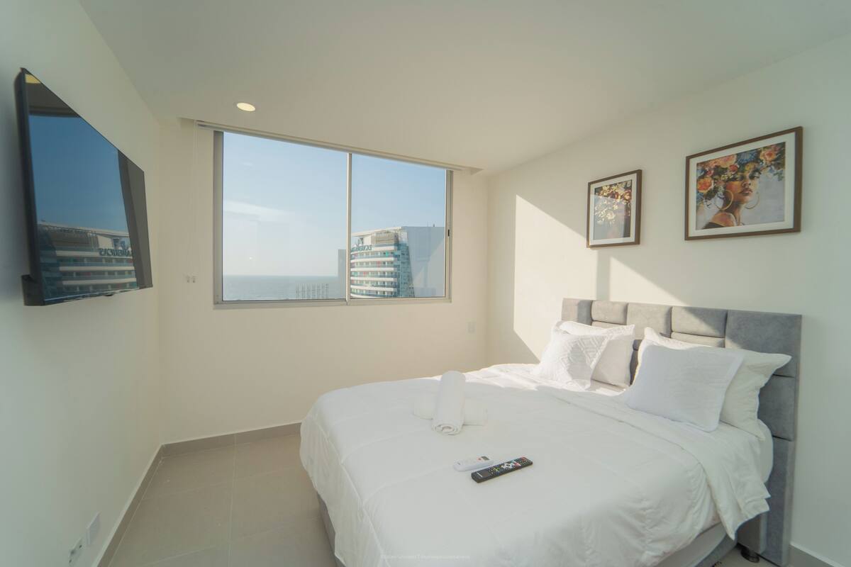 Une chambre d’hôtel moderne dotée d’un grand lit, d’un téléviseur à écran plat fixé au mur et d’une fenêtre donnant sur la ville.
