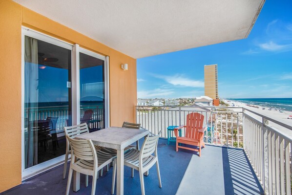 A balcony with a table and chairs, a view of the beach, and a tall building in the distance.