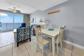 A dining area with a table and chairs, a ceiling fan, and a view of the sea. - Splash 1802e (Panama City Beach)