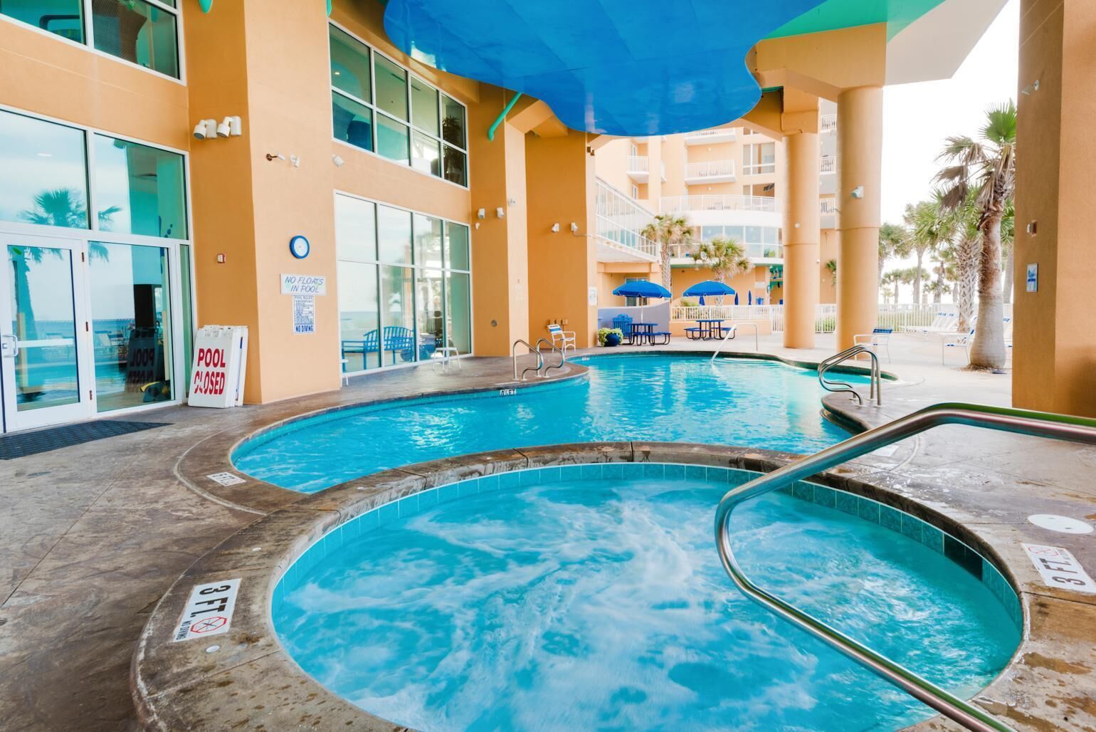Un área de piscina con dos jacuzzis, una zona de estar cubierta y un letrero de cierre de piscina.