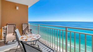 Ein Balkon mit Blick auf das Meer, ein runder Tisch mit gemustertem Tuch, zwei Stühle und eine kleine Wandleuchte.