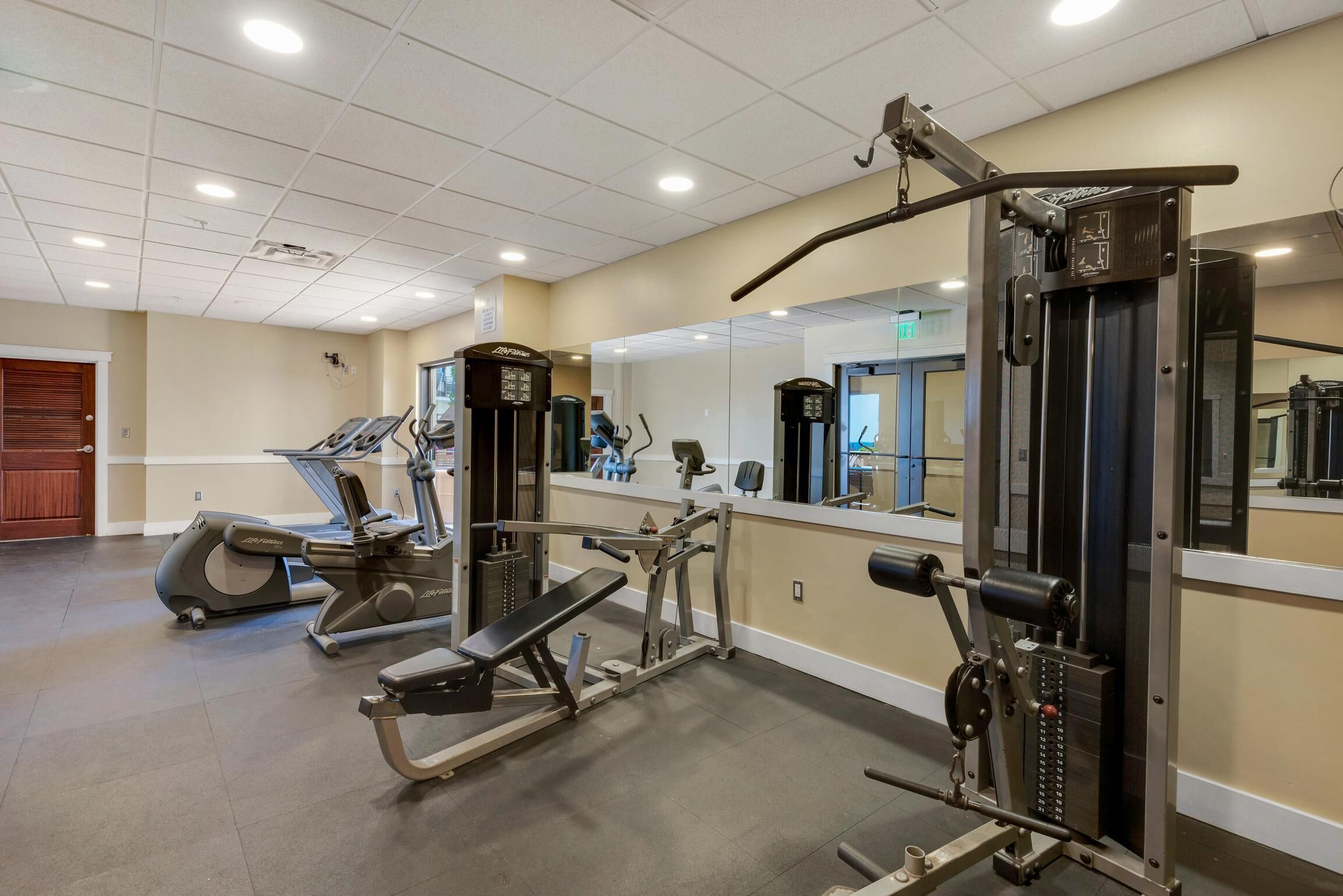 Un gimnasio con máquinas de cardio, equipo de levantamiento de pesas y un espejo grande.