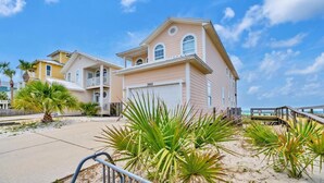 A beachfront property with a large house, a covered driveway, and a wooden walkway leading to the beach.