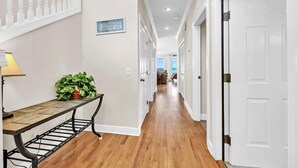 A hallway with wooden flooring, white walls, and a staircase with white balusters.