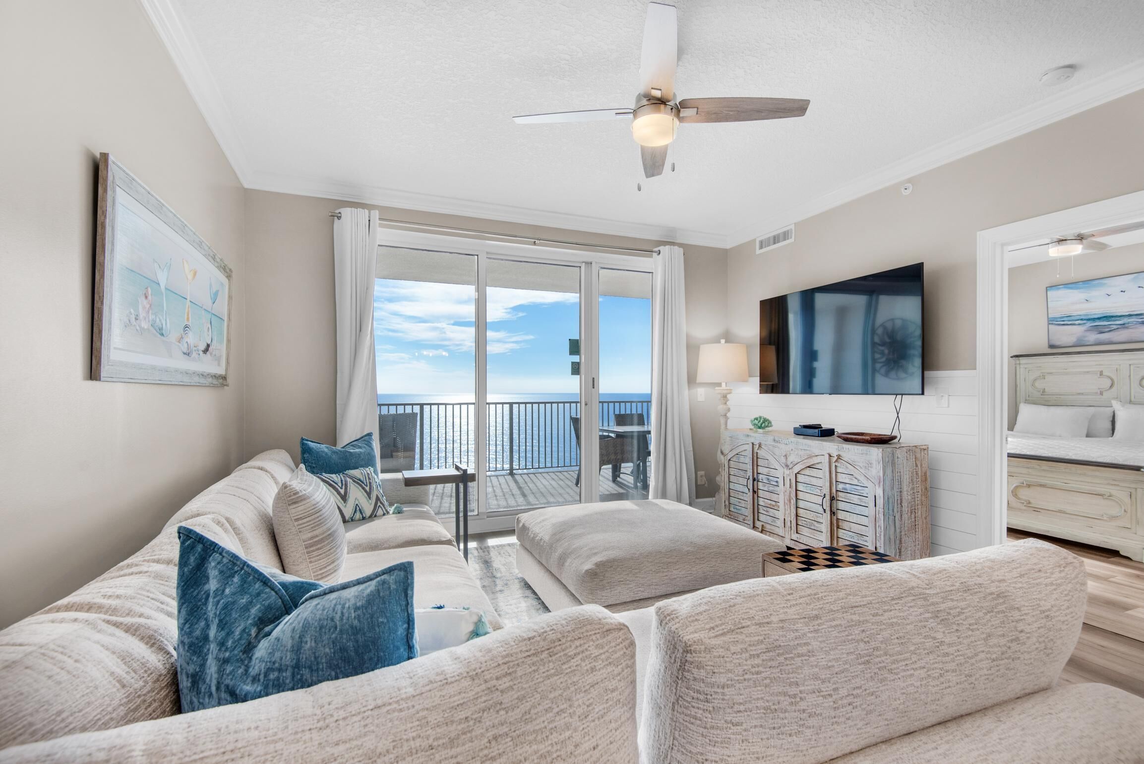 A spacious living area with a balcony, a ceiling fan, and a television.