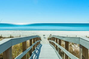 Une promenade en bois qui mène à une plage aux eaux d’un bleu limpide.